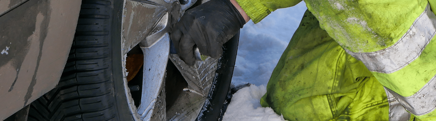 Image of an auto technician changing a flat tire on the side of the road in winter