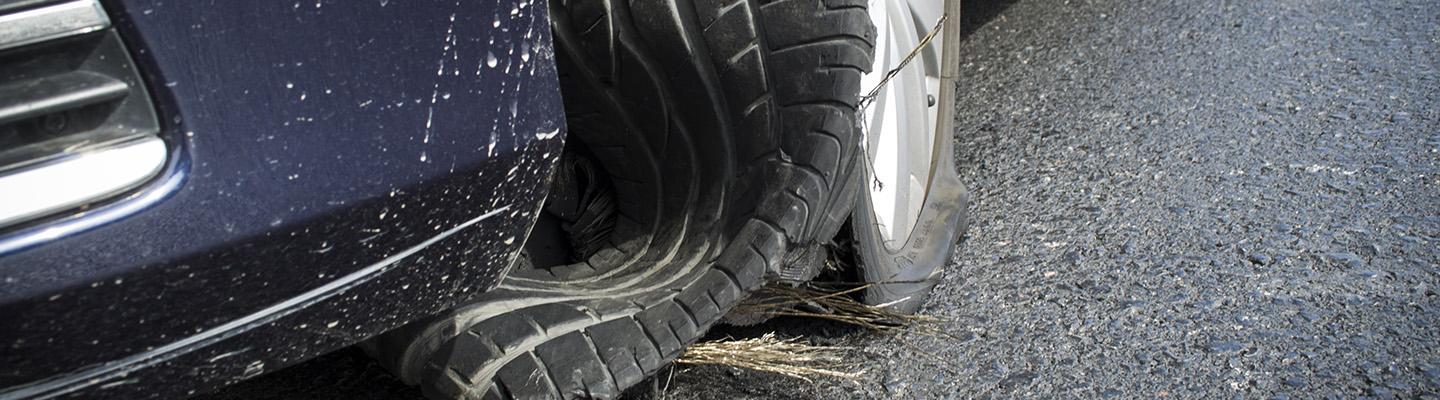 Close-up of a car with a flat tire on a wet road, showing a severely damaged rubber tread.